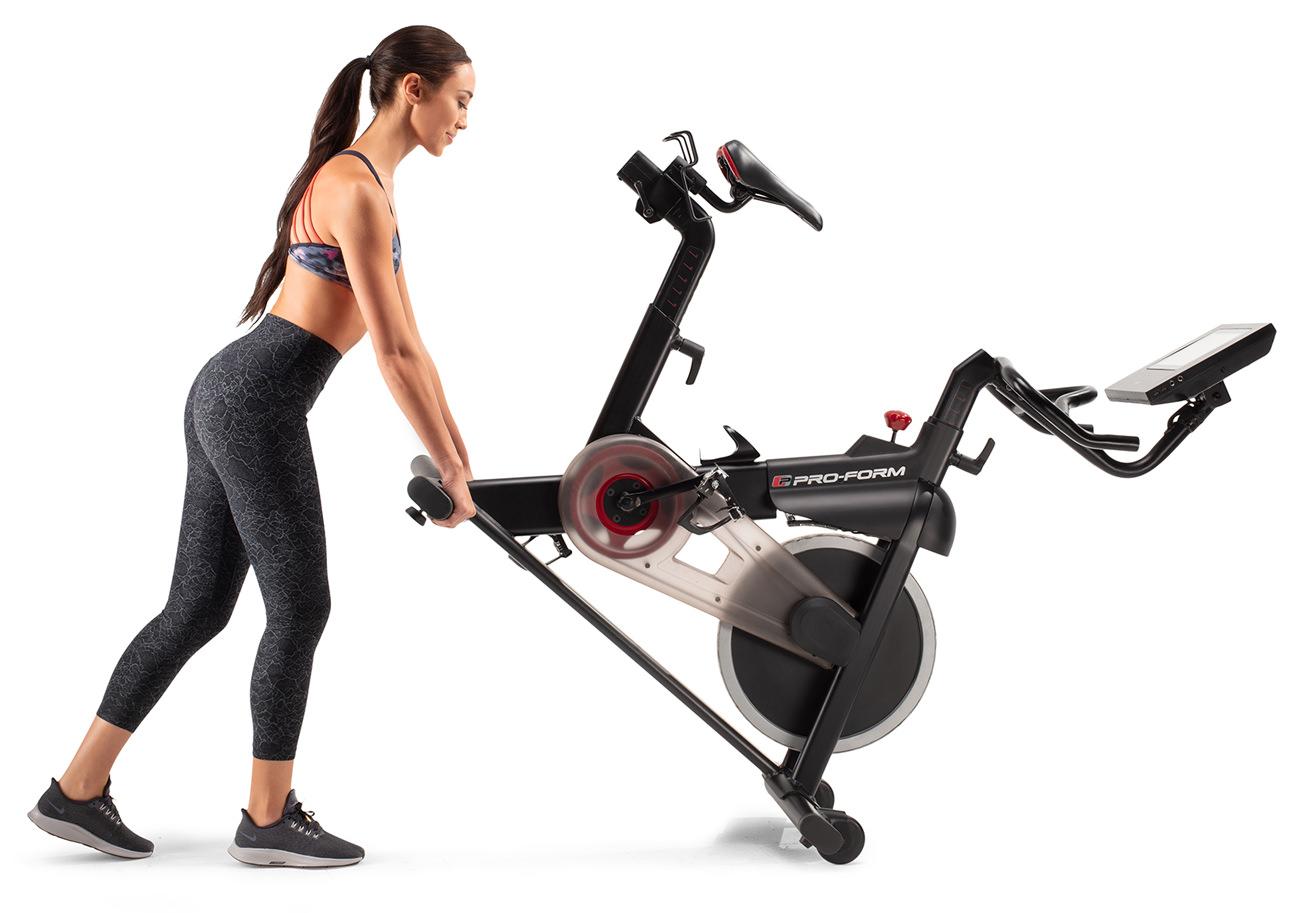 A woman moving an exercise bike using its roller wheels.